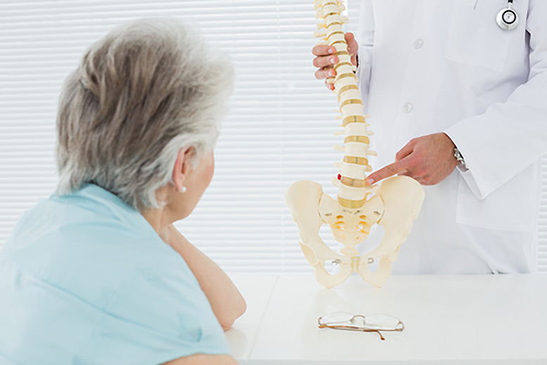 Osteopath pointing to a spinal skeleton as an elderly woman watches